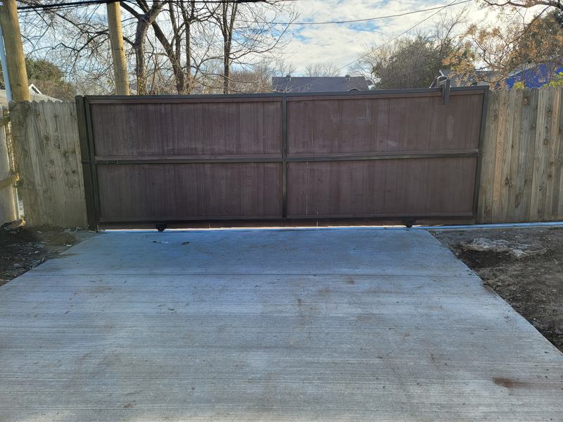 Fresh broom-finish concrete drive leading to a brown wooden rolling gate between two wood fences