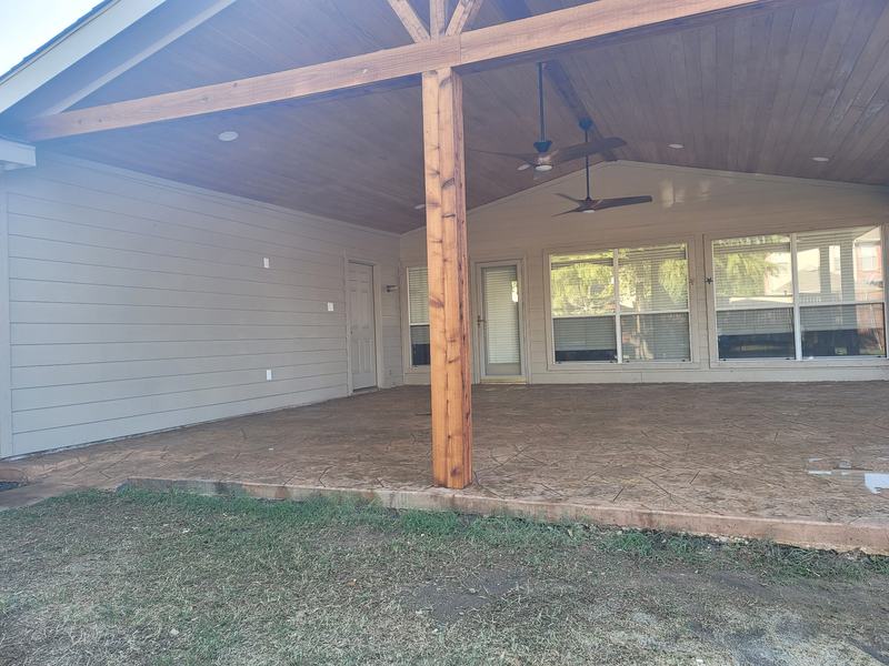 Covered back patio with a wood post, plank ceiling, ceiling fans and a textured concrete floor
