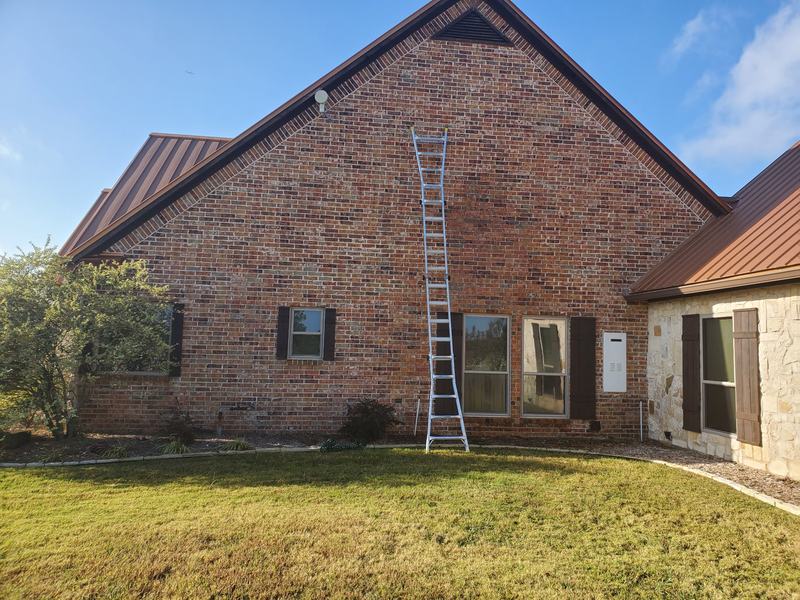 Brick home with a new brown metal roof and an extension ladder leaning against the gable wall