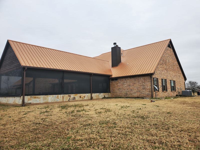 Corner of a home with a copper-colored metal roof, brick chimney and a screened porch along the side