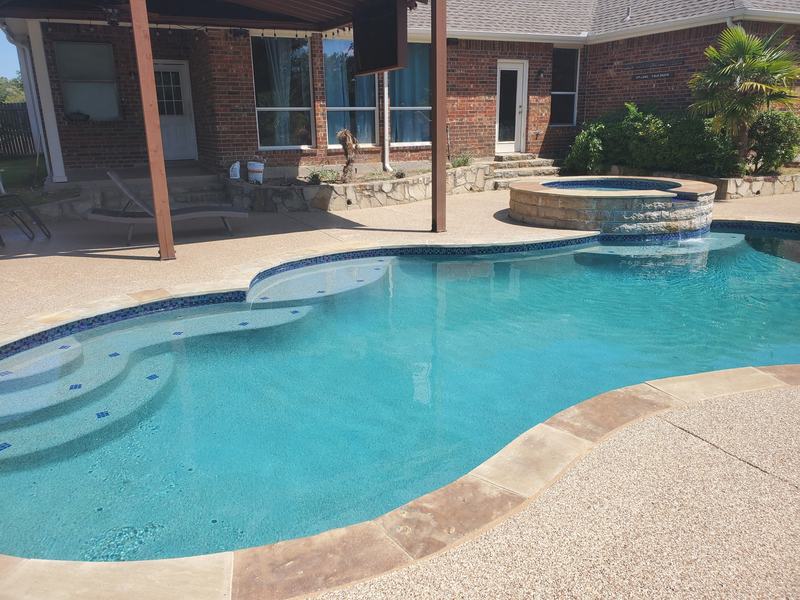 Refilled backyard pool with clear blue water, a raised stone spa and a new light speckled deck