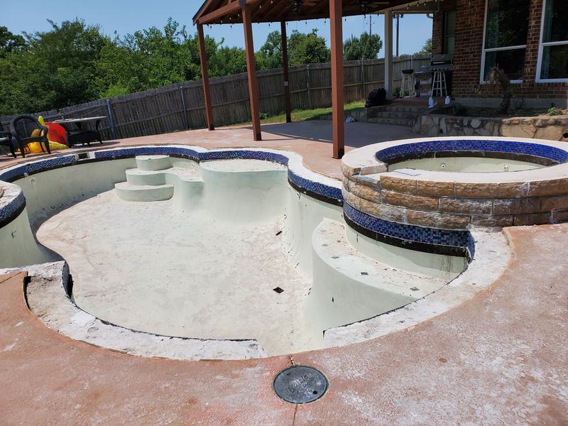 Drained backyard pool and raised stone spa with worn plaster and a stained concrete deck