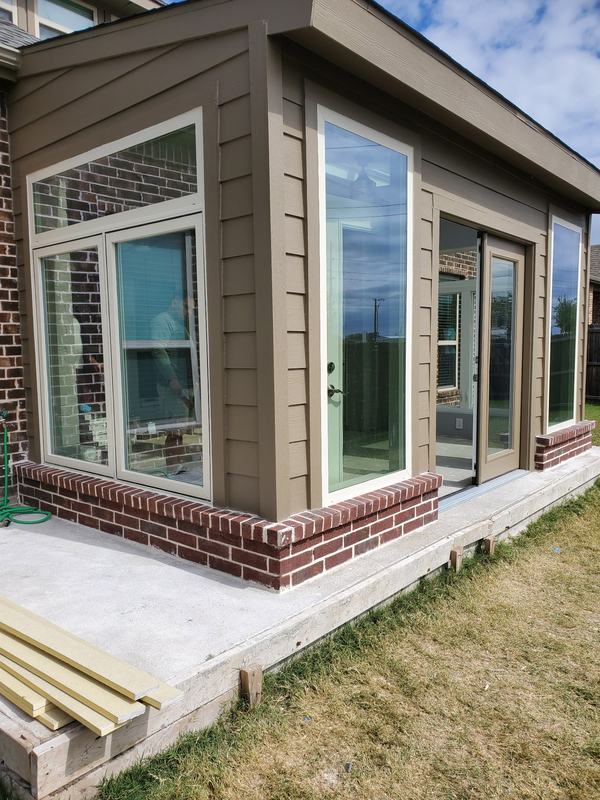 New sunroom attached to a brick home with tall windows, siding and a brick knee wall